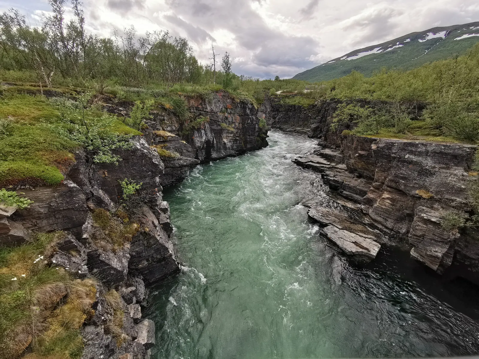 Der türkisgrüne Abiskojåkka fließt durch einen schmalen Canyon aus geschichtetem Fels im Abisko-Nationalpark, am Rand Birkengebüsch
