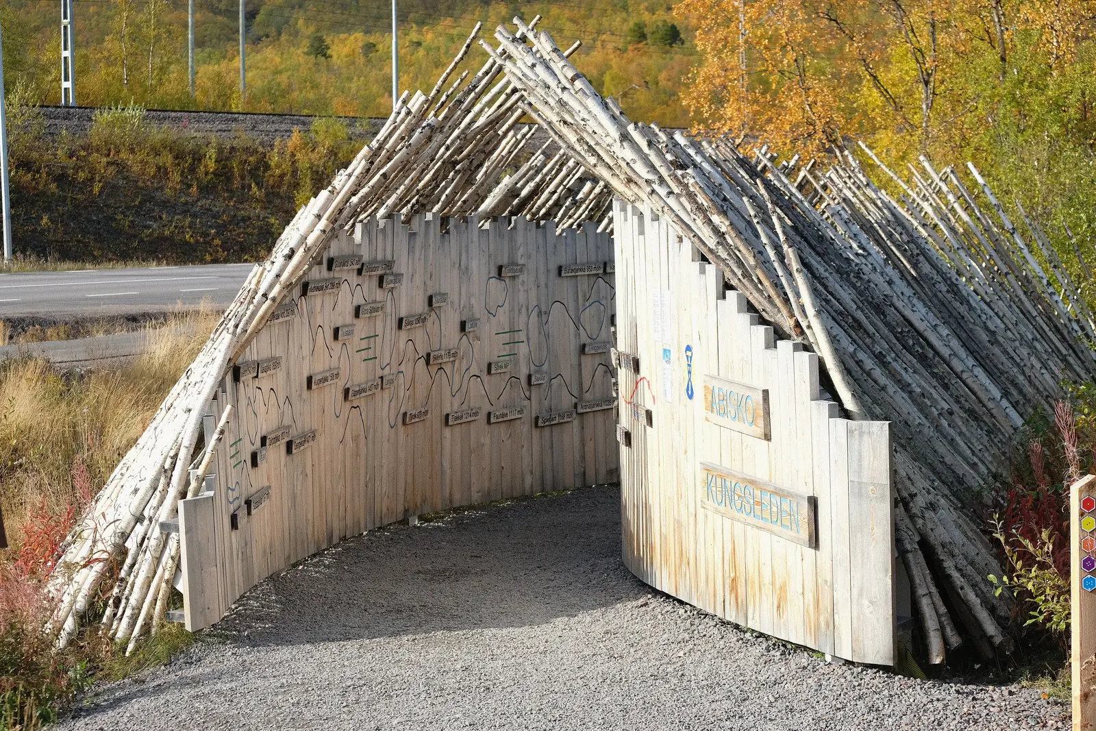 Das hölzerne Eingangstor mit der Aufschrift Kungsleden am Start des Fernwanderwegs bei der Abisko Turiststation, umgeben von herbstlichem Birkenlaub