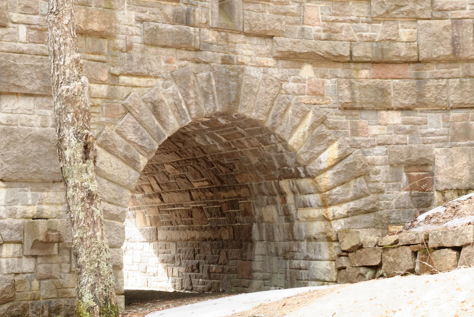 Steinbogenbrücke aus rosa Granitquadern über einem Carriage-Road-Abschnitt im Acadia-Nationalpark