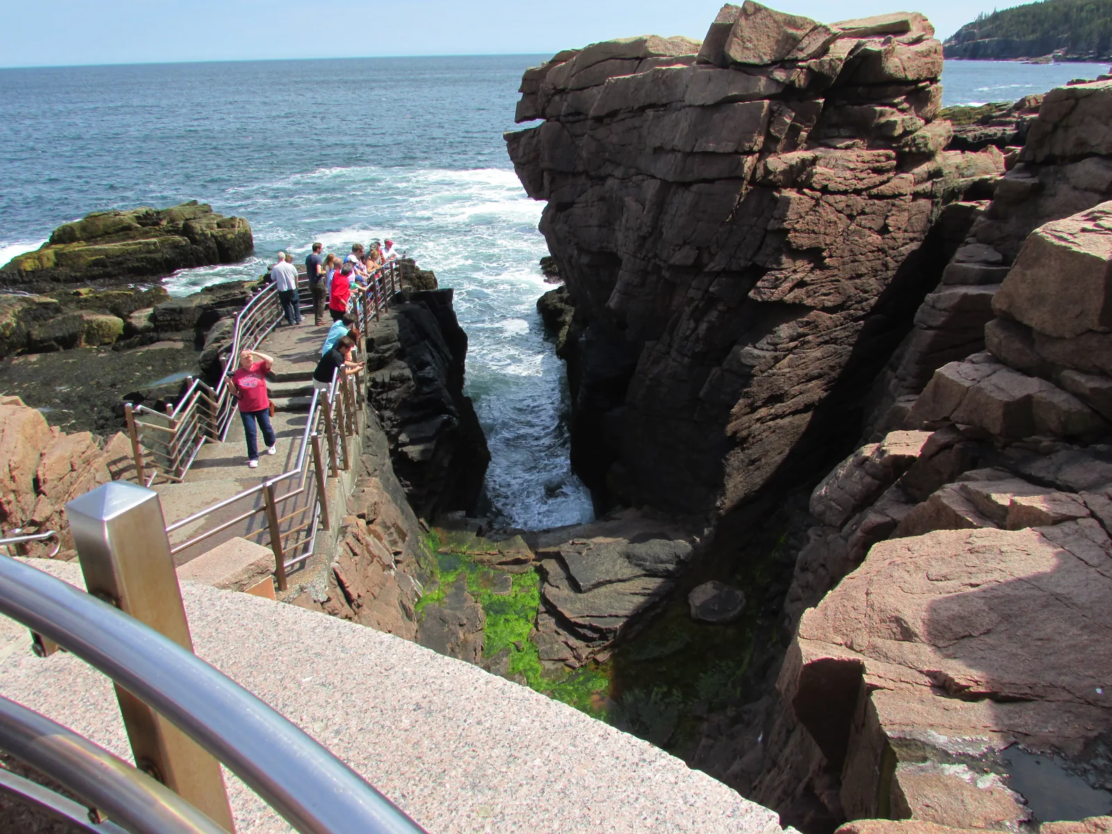 Besucher auf dem Steg über dem Felsspalt Thunder Hole, in den eine Welle aus dem Atlantik schlägt