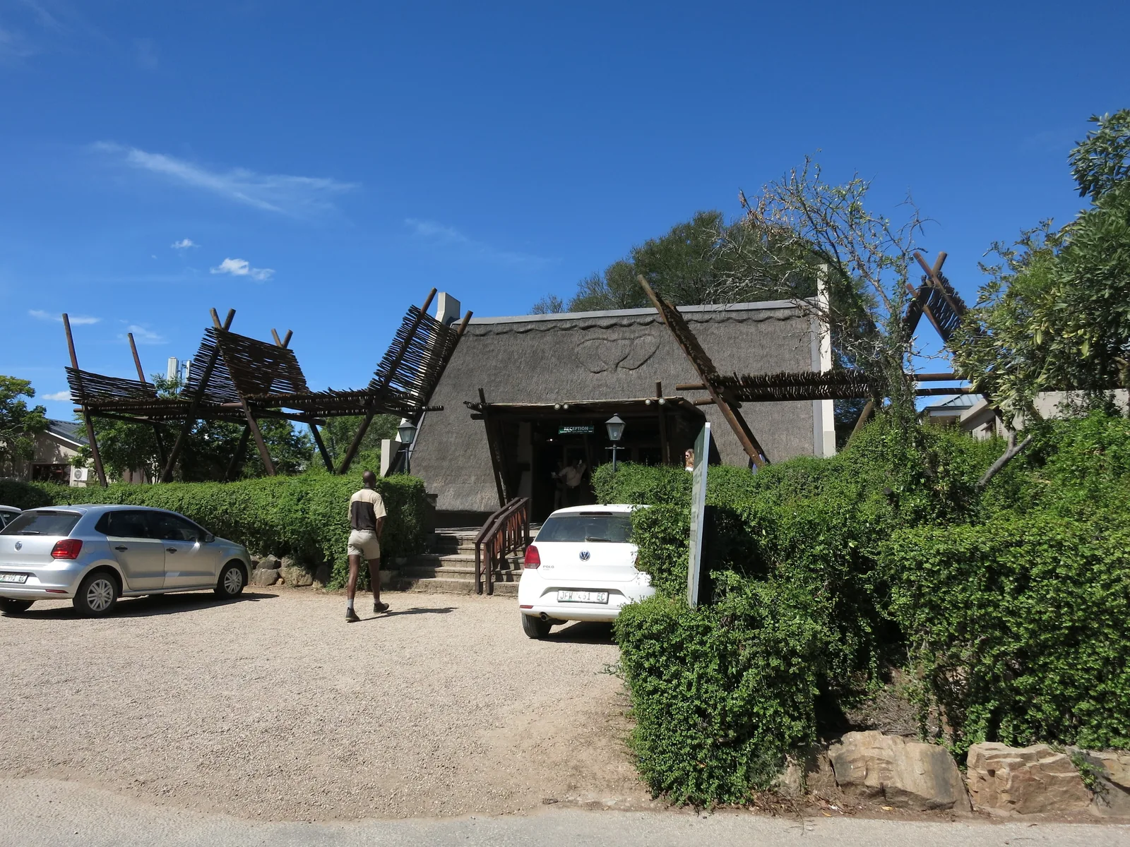 Reetgedecktes Gebäude im Addo Main Camp des Addo-Elephant-Nationalparks, davor Autos und Büsche