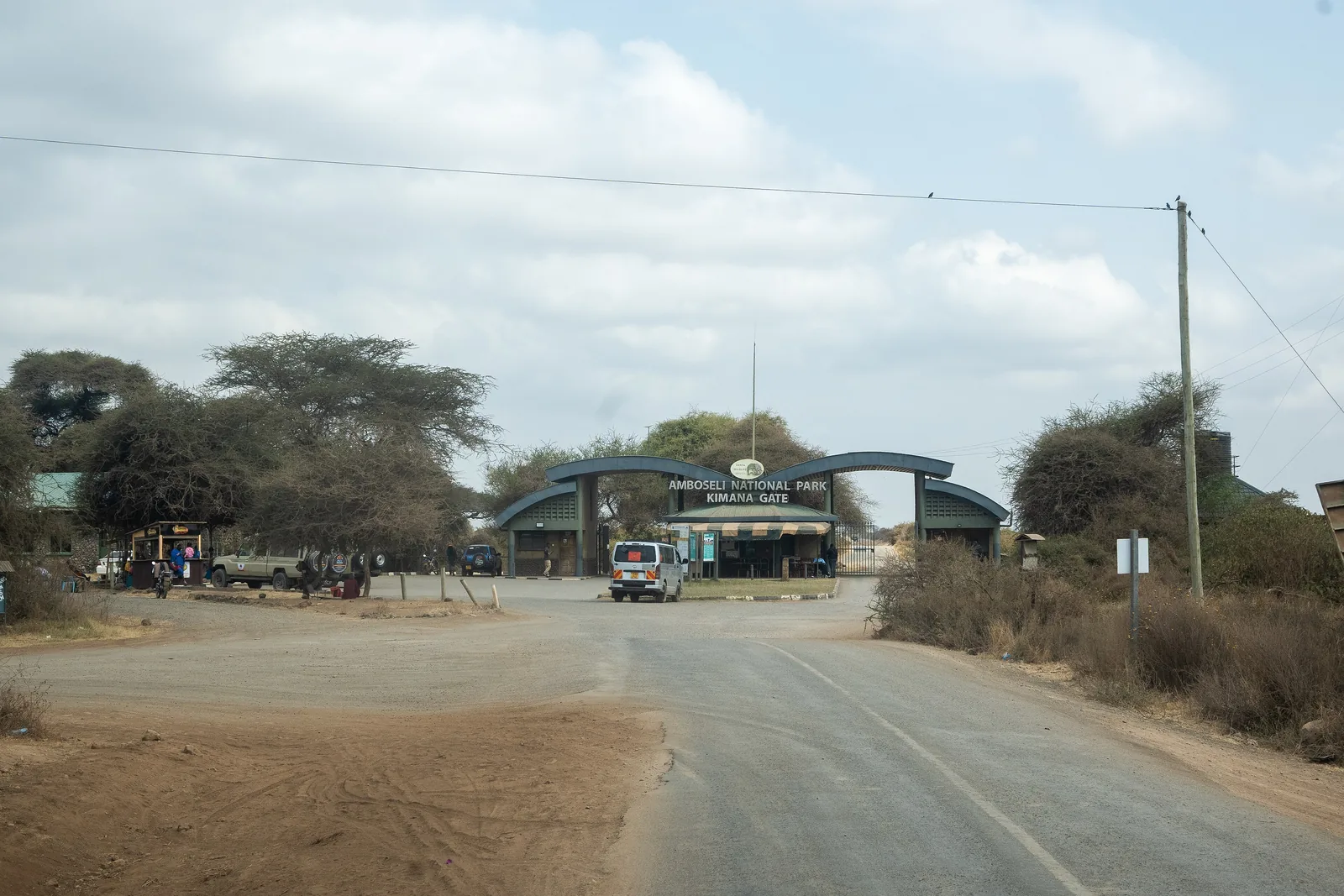 Die Zufahrtsstraße zum Kimana Gate des Amboseli-Nationalparks, am Ende der Straße das Torgebäude zwischen Akazien