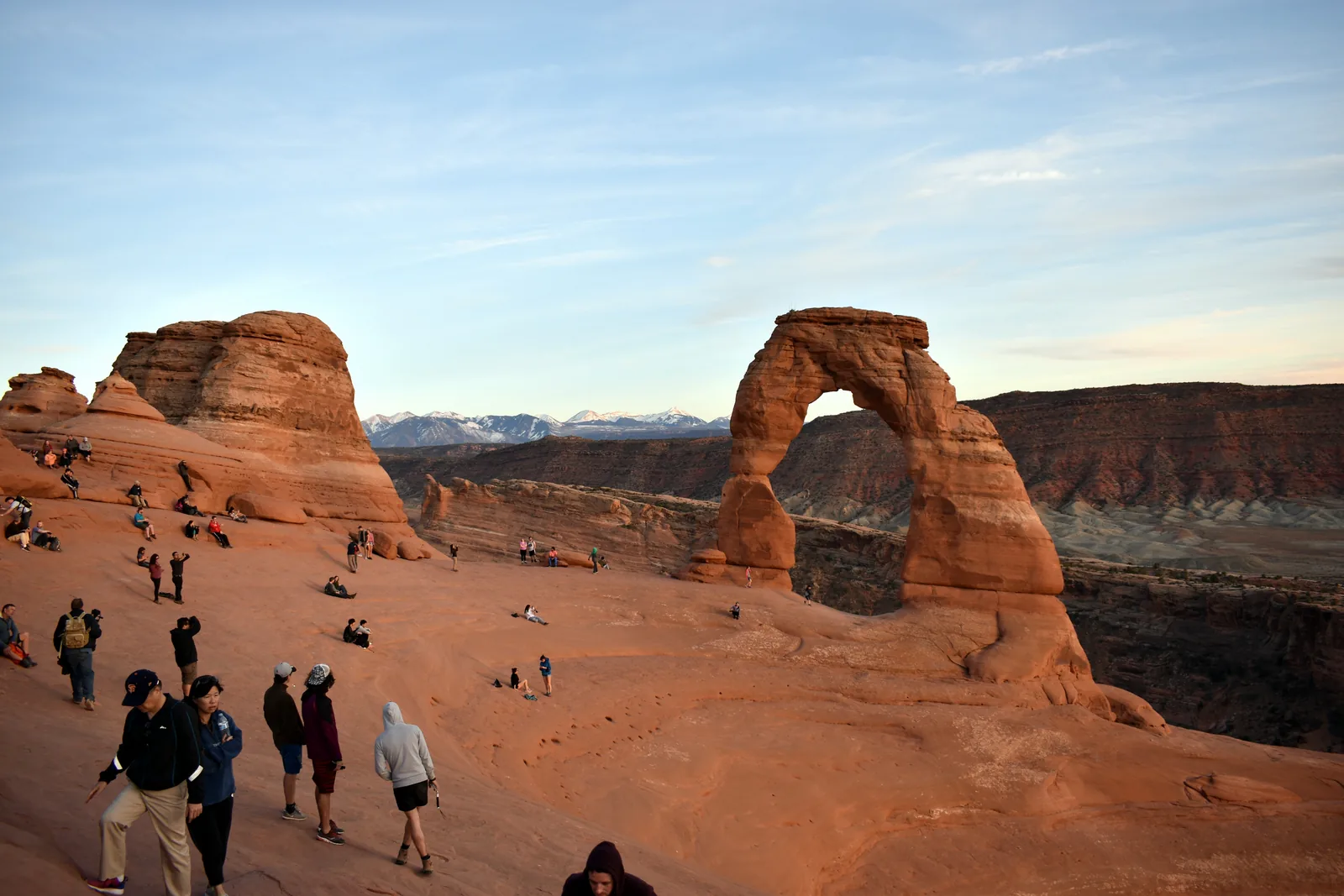 Dutzende Menschen sitzen und stehen in der Felsmulde vor dem Delicate Arch und warten auf den Sonnenuntergang