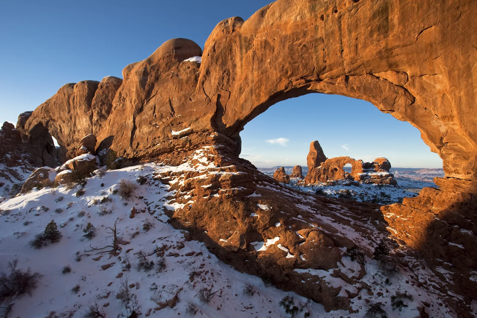 Turret Arch, eingerahmt von der Öffnung des North Window, im ersten Morgenlicht über verschneitem Boden