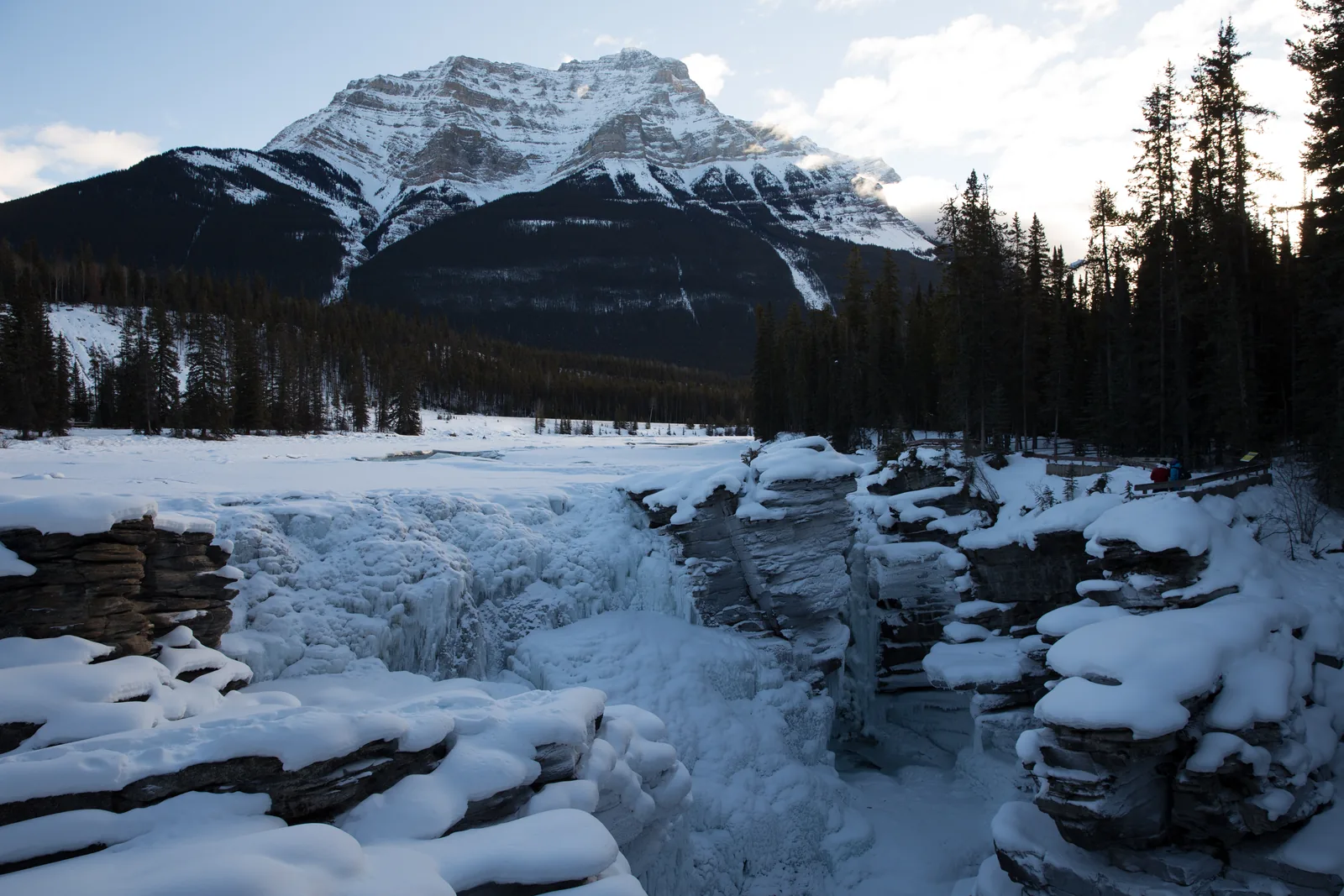 Die vereisten Athabasca Falls im Jasper-Nationalpark unter Schnee, dahinter ein verschneiter Berg