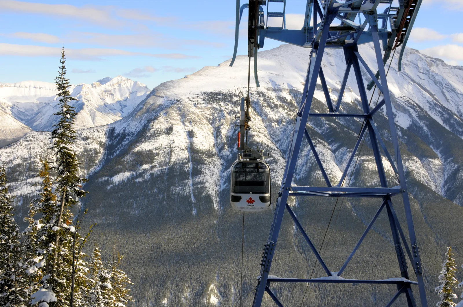 Gondelkabine mit Ahornblatt an einem blauen Stahlmast vor verschneiten Bergen