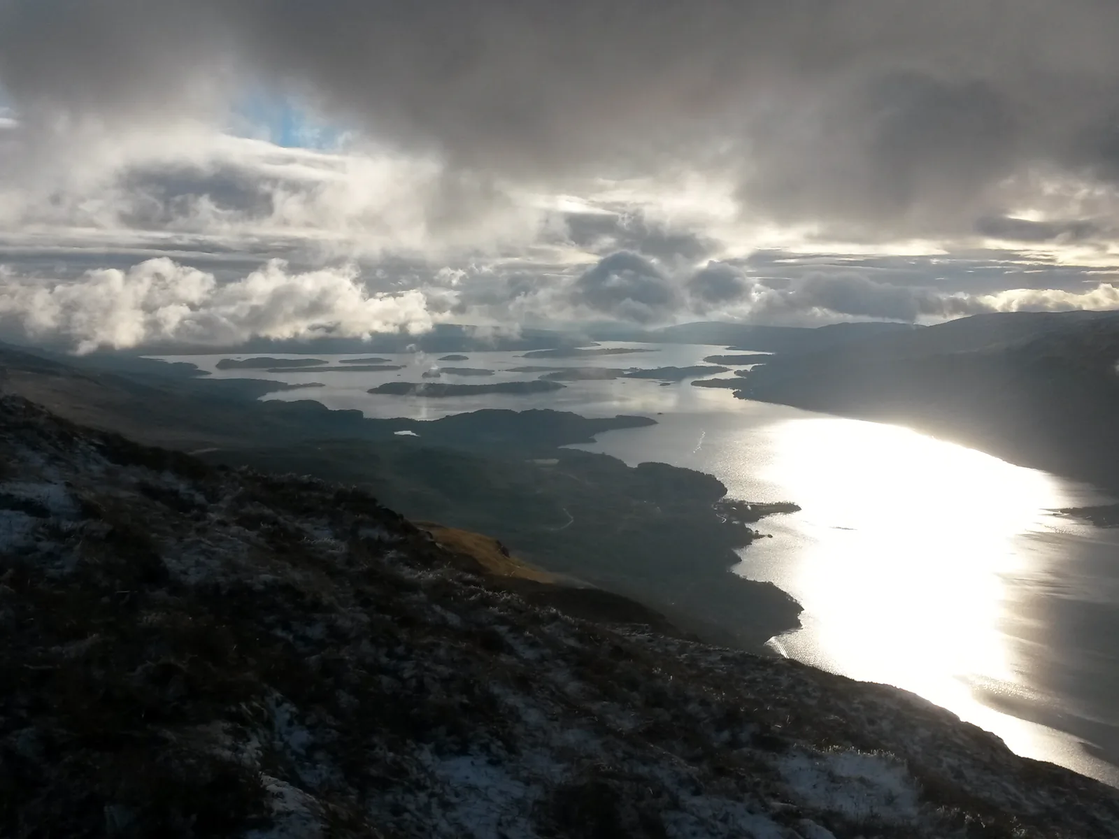 Blick von den Hängen des Ben Lomond im Loch-Lomond-and-The-Trossachs-Nationalpark auf den glitzernden Loch Lomond unter Wolken