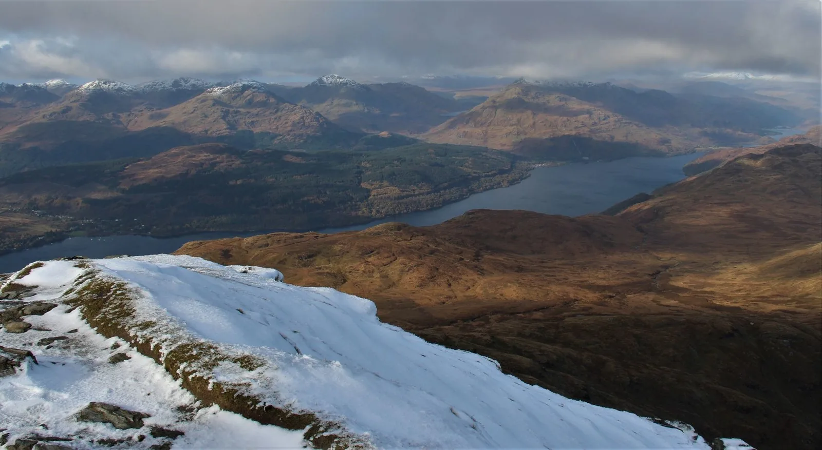 Verschneiter Hang am Ben Lomond mit Blick über den Loch Lomond auf die Berge der Arrochar Alps
