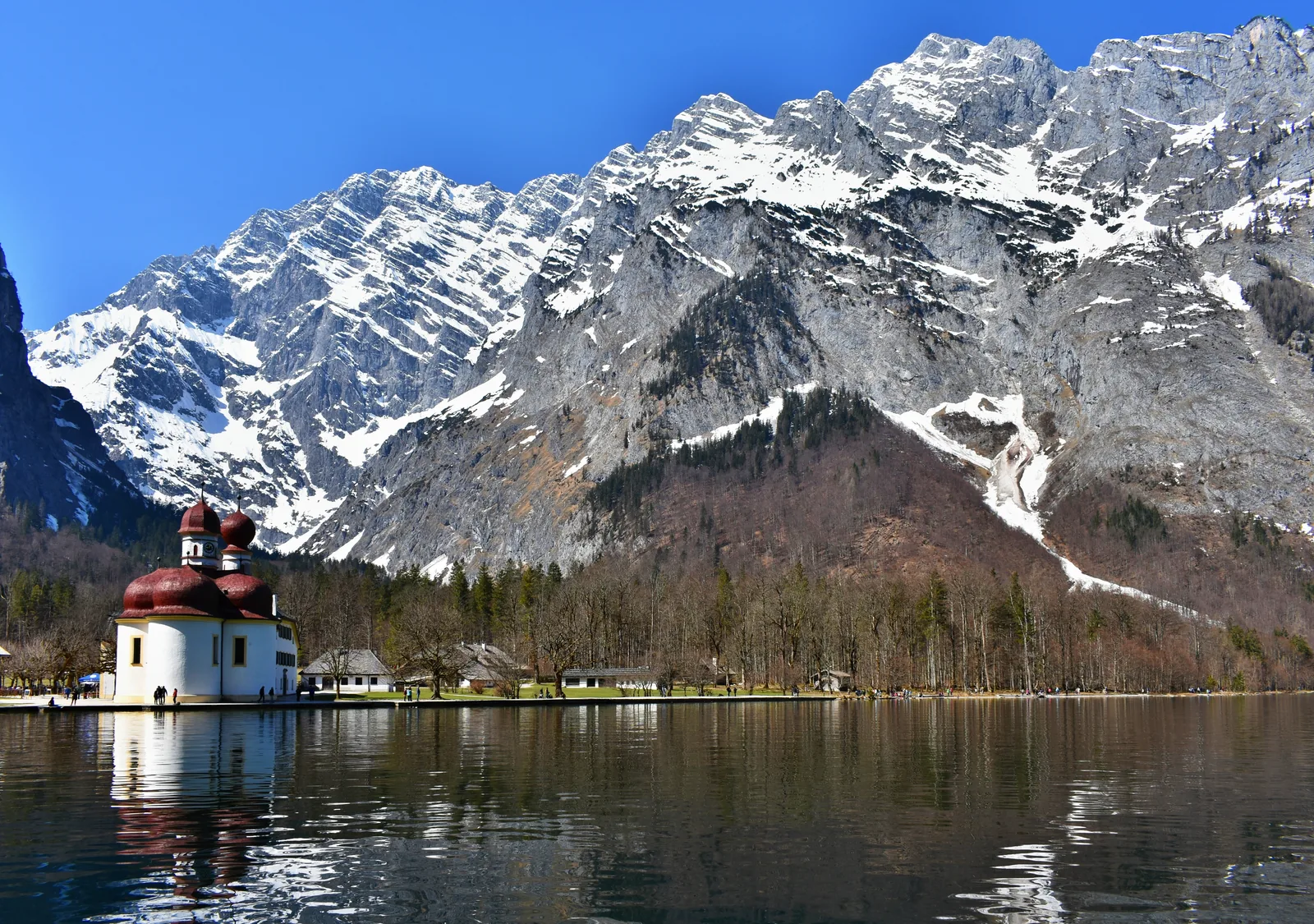 Die rote Kuppelkirche St. Bartholomä am Königssee vor der verschneiten Watzmann-Ostwand