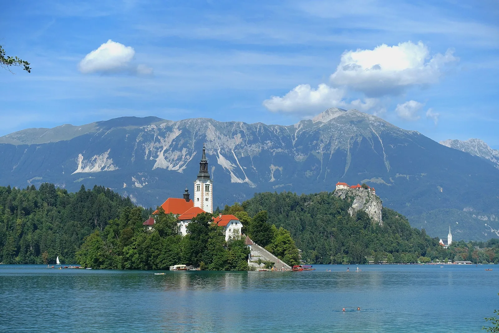 Bleder Insel mit der Wallfahrtskirche, dahinter die Burg Bled auf dem Felsen und die Berge der Karawanken