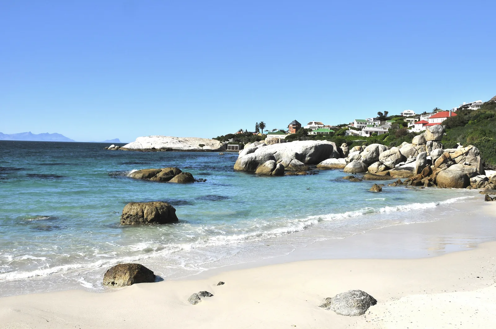 Foxy Beach am Boulders Beach mit weißem Sand, runden Granitfelsen und klarem Wasser, im Hintergrund Häuser von Simon’s Town