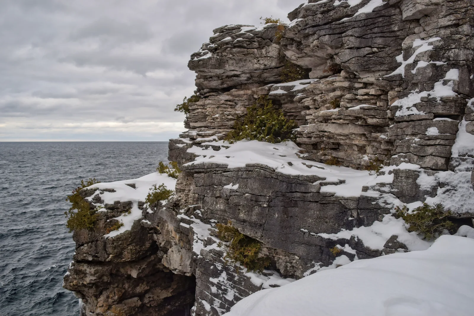 Verschneite, waagerecht geschichtete Kalksteinklippen brechen zur dunklen Georgian Bay ab, in den Felsspalten wachsen verdrehte Zedern