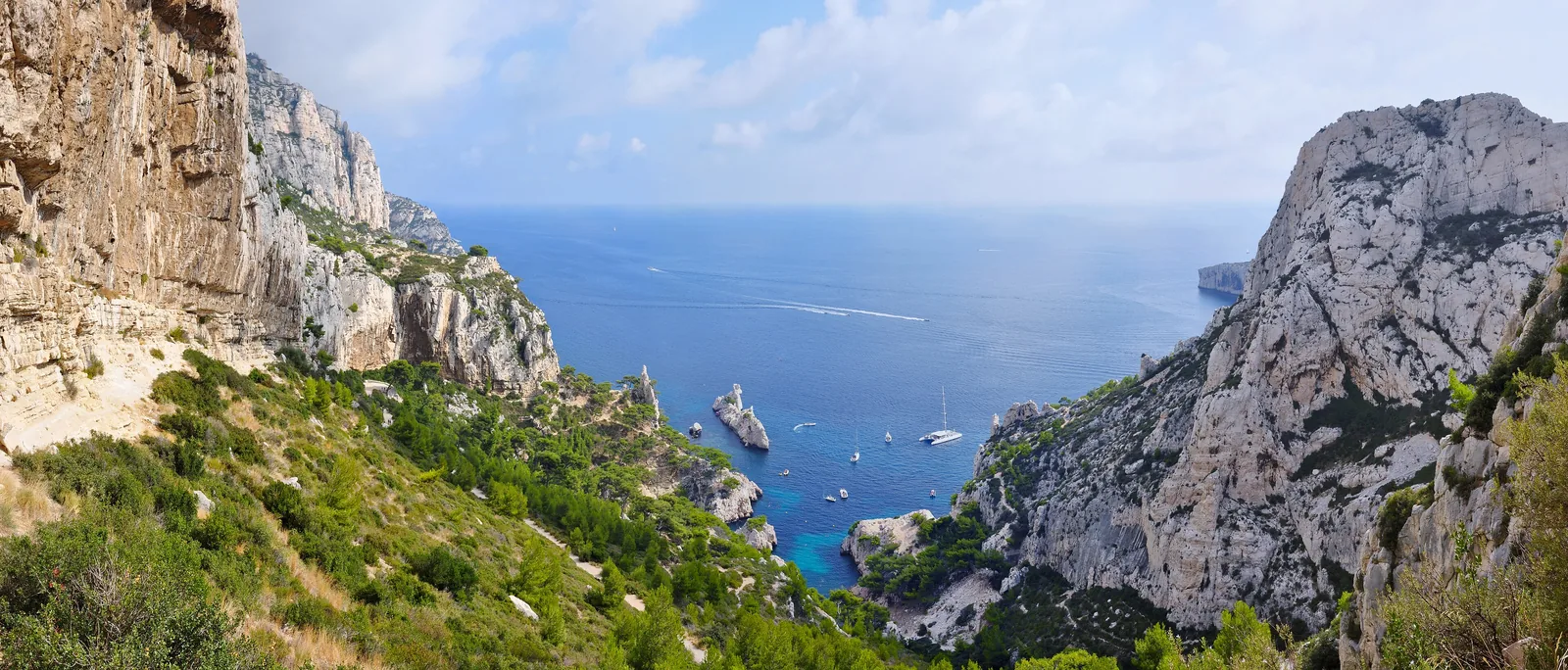 Panorama in die Calanque de Sugiton im Nationalpark Calanques vom Wanderweg: Kalkfelsen, grüne Hänge und Boote im blauen Wasser
