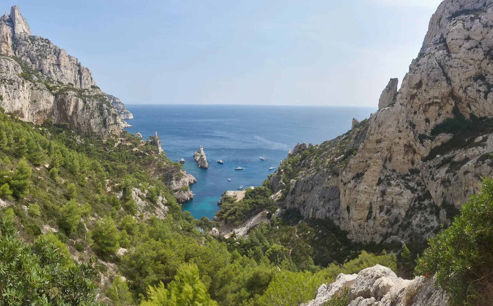 Blick vom Weg hinab zur Calanque de Sugiton im Nationalpark Calanques: grüne Hänge, Kalkfelsen und das Inselchen Le Torpilleur im türkisen Wasser