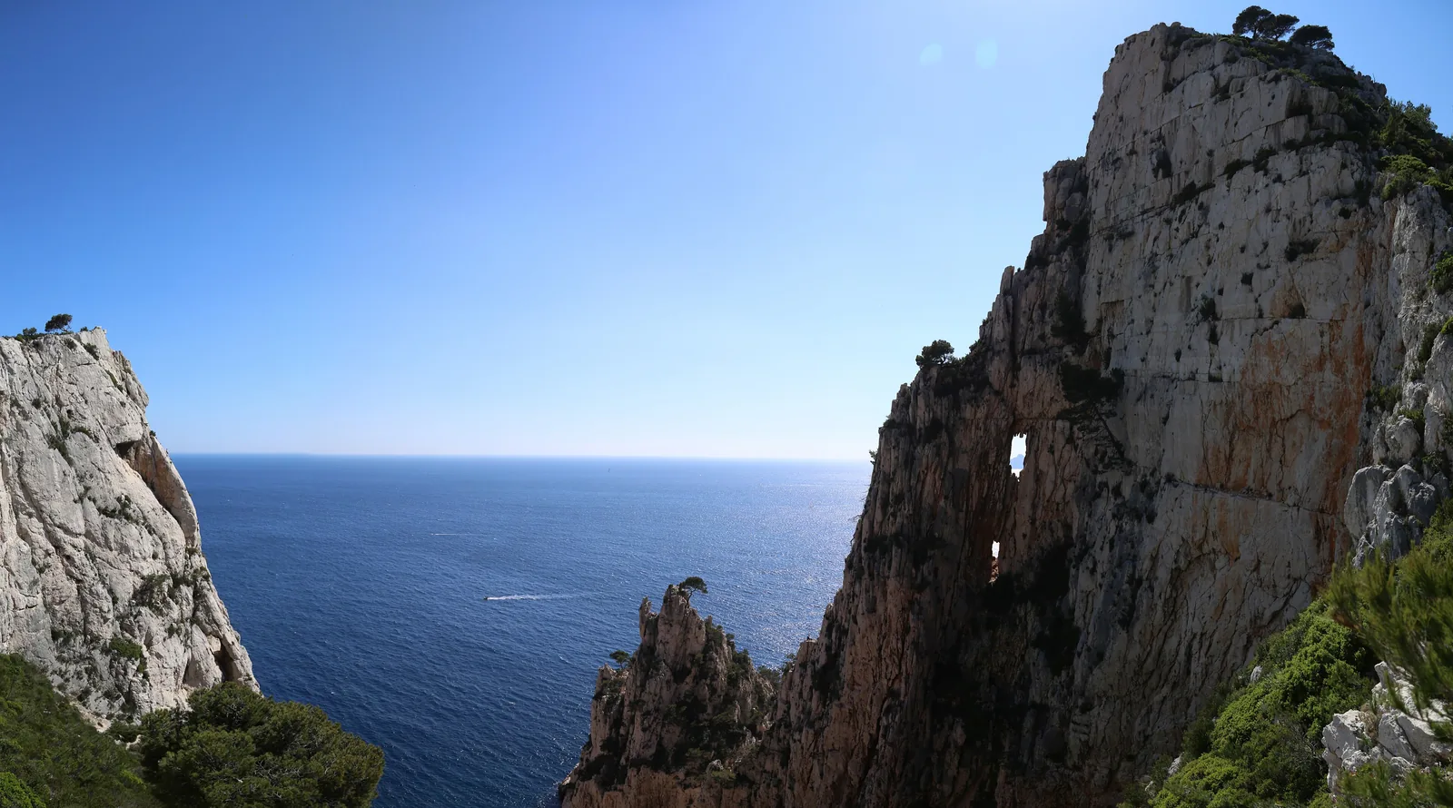Eine Kalkwand mit natürlichem Felsloch an der Calanque d’En-Vau im Nationalpark Calanques, dahinter das offene Meer