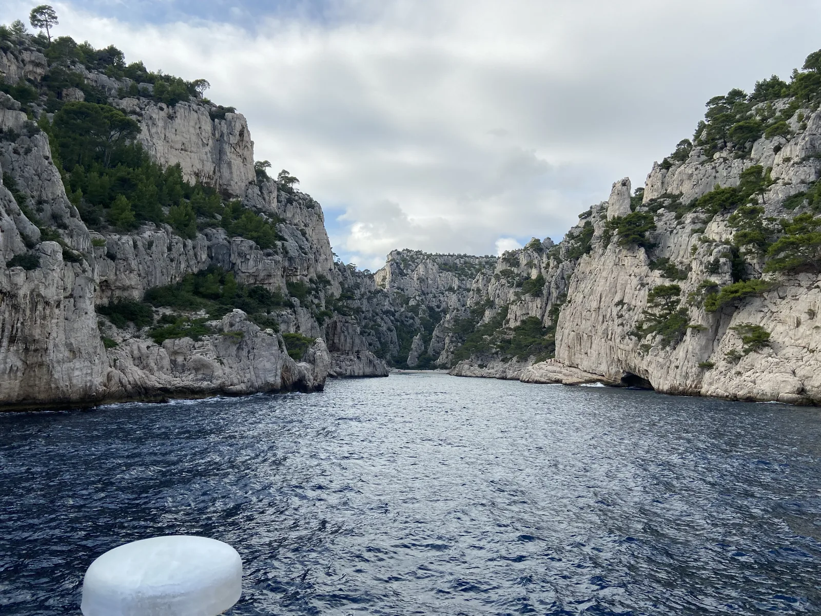 Blick von einem Ausflugsboot in die Calanque d’En-Vau im Nationalpark Calanques: dunkles Wasser zwischen bewaldeten Kalkwänden