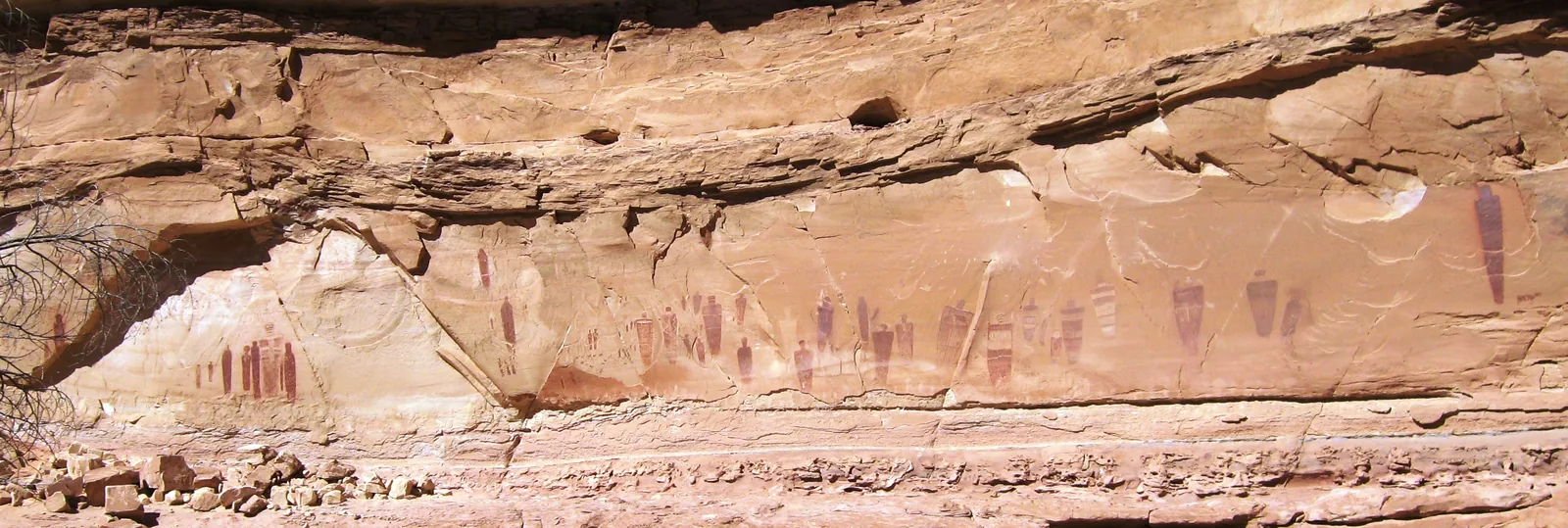 Reihe dunkelroter, lebensgroßer Figuren auf heller Sandsteinwand im Horseshoe Canyon