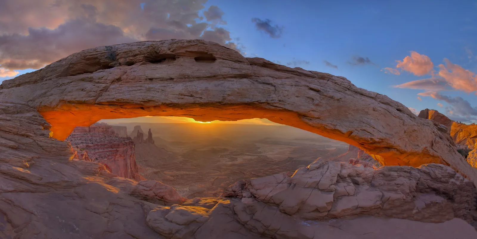 Der Mesa Arch im Gegenlicht des Sonnenaufgangs, die Unterseite des Bogens glüht orange über der Cañonlandschaft