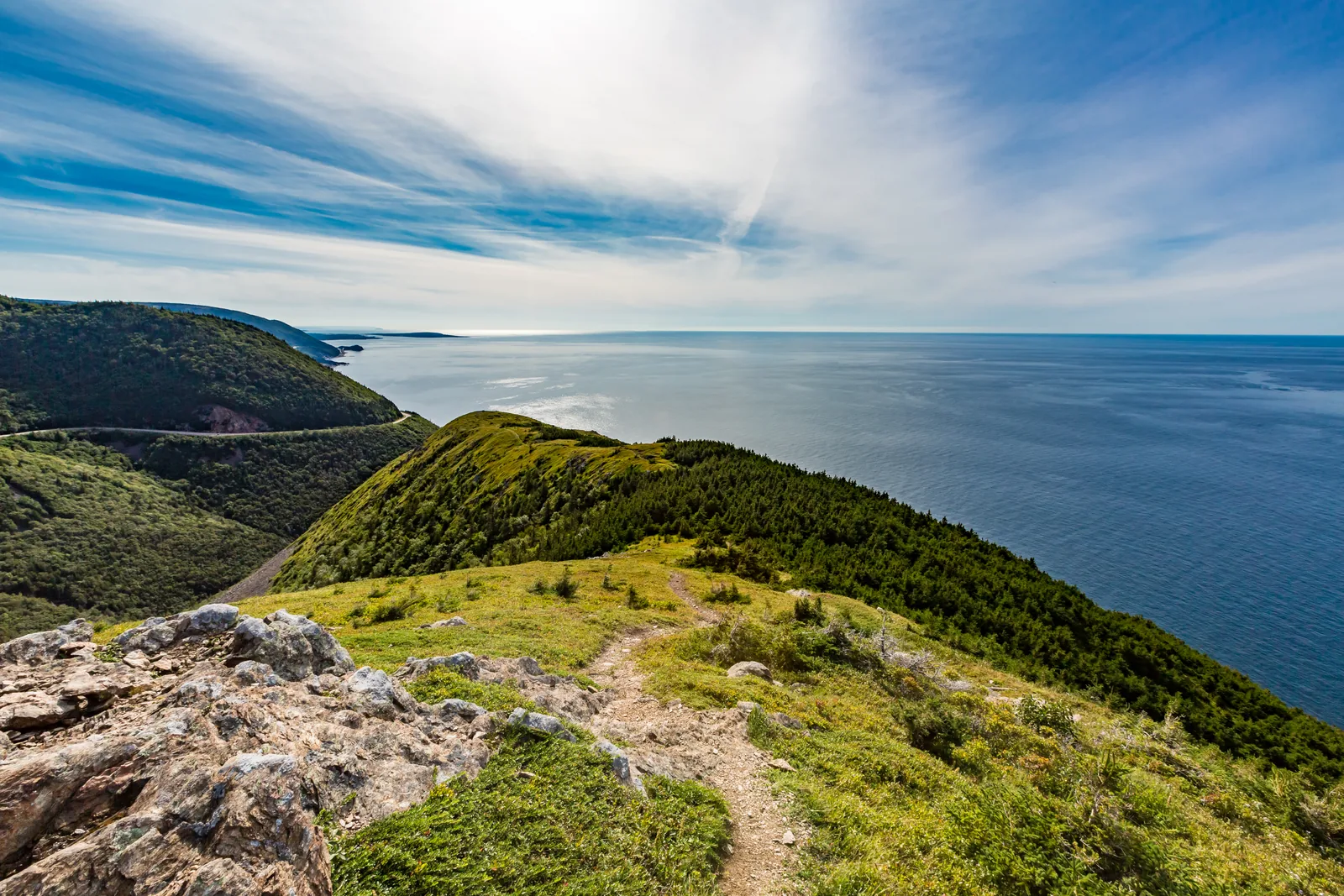 Blick vom Ende des Skyline Trail: ein grüner Bergrücken fällt zum Meer ab, links windet sich der Cabot Trail an der Küste entlang
