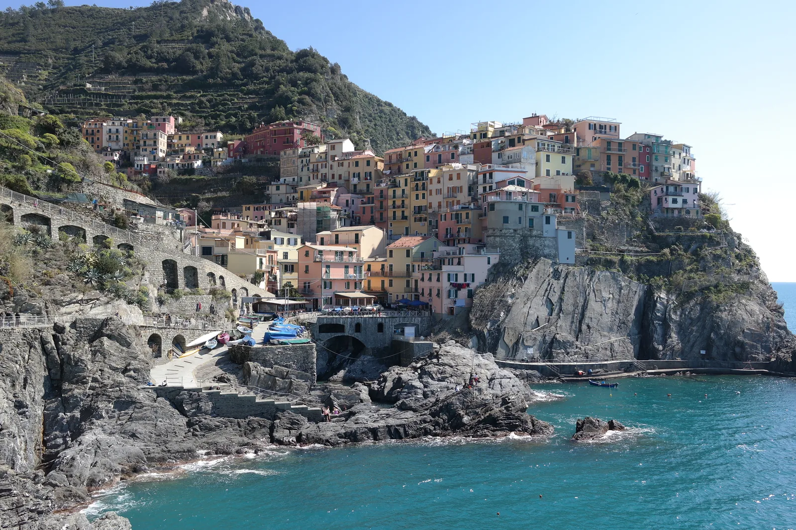 Manarola im Nationalpark Cinque Terre: bunte Häuser auf einem dunklen Felsrücken über dem Meer, dahinter Weinbergterrassen