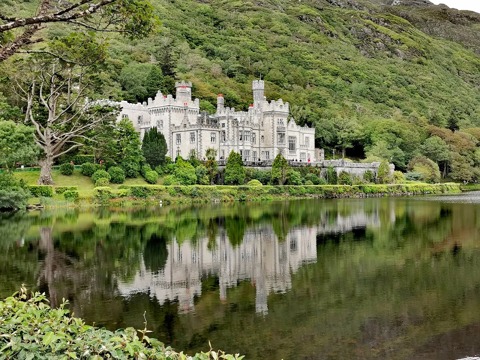Die Kylemore Abbey nahe dem Connemara-Nationalpark am Ufer eines Sees vor bewaldetem Hang