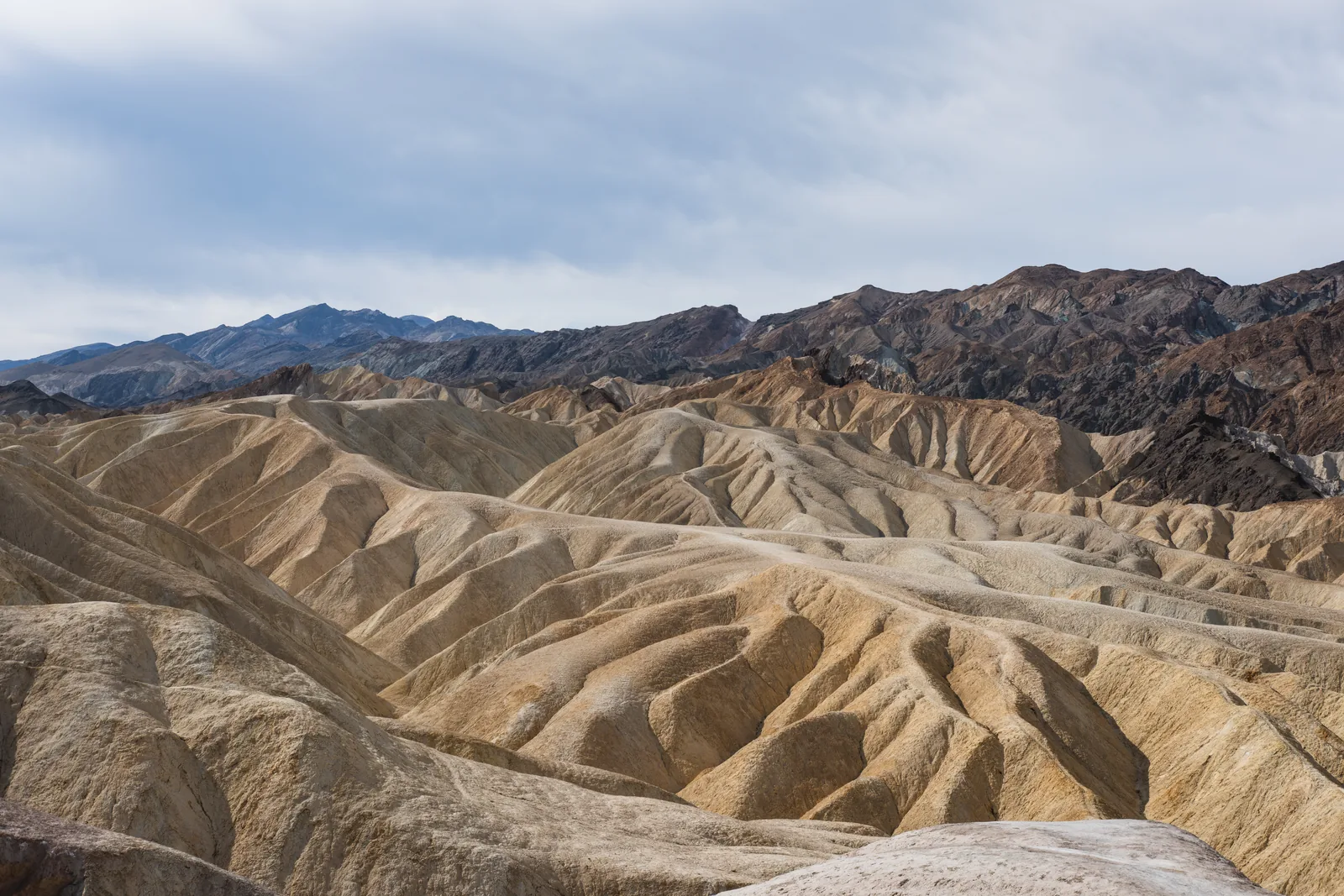 Fein zerfurchte gelb-braune Badlands unter den dunklen Kämmen der Amargosa Range