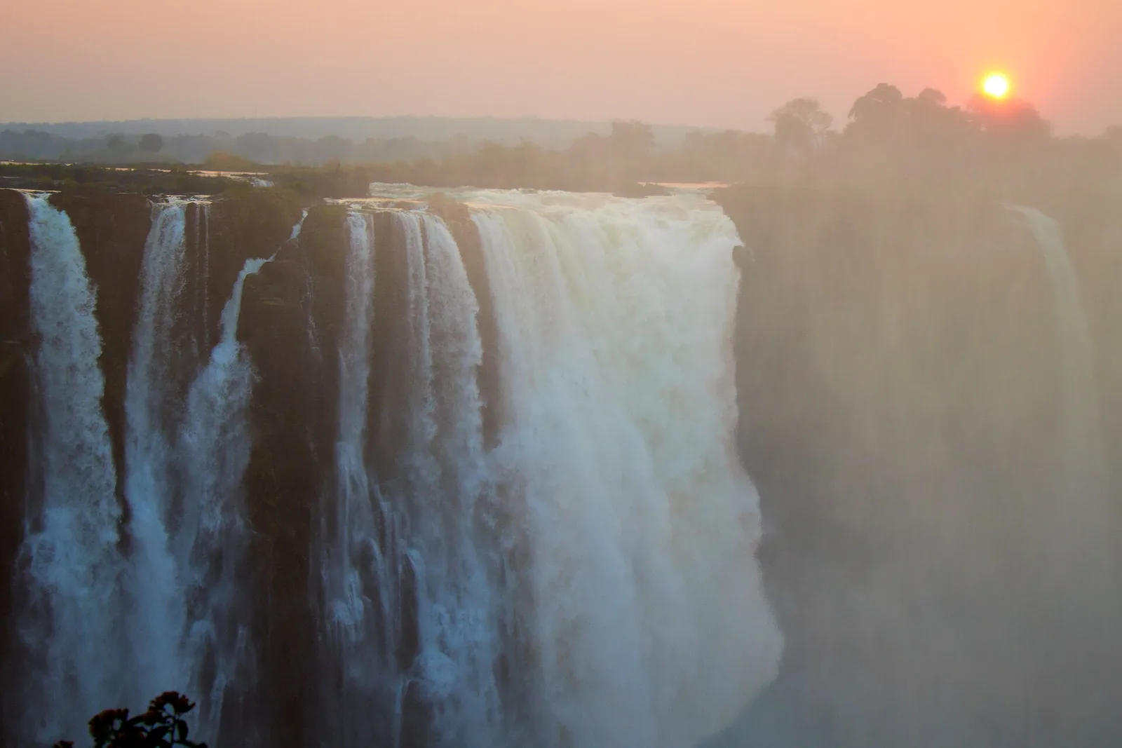 Die Victoria Falls im Abendlicht, Wasser stürzt über die Kante, und die Gischt leuchtet vor der tief stehenden Sonne