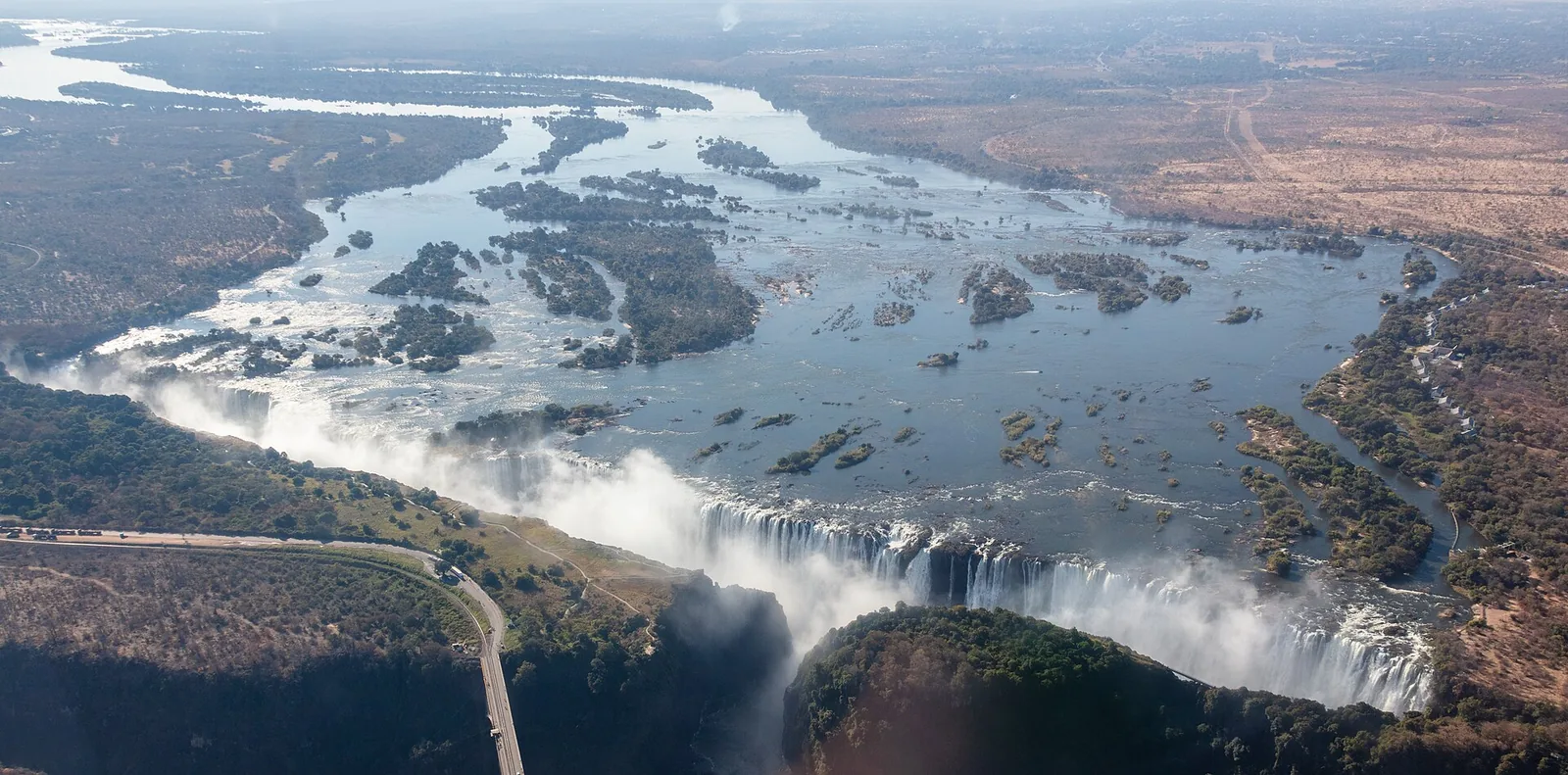 Luftbild der Victoria Falls mit Livingstone Island an der Kante, wo der Devil's Pool liegt, dahinter der Sambesi mit seinen Inseln
