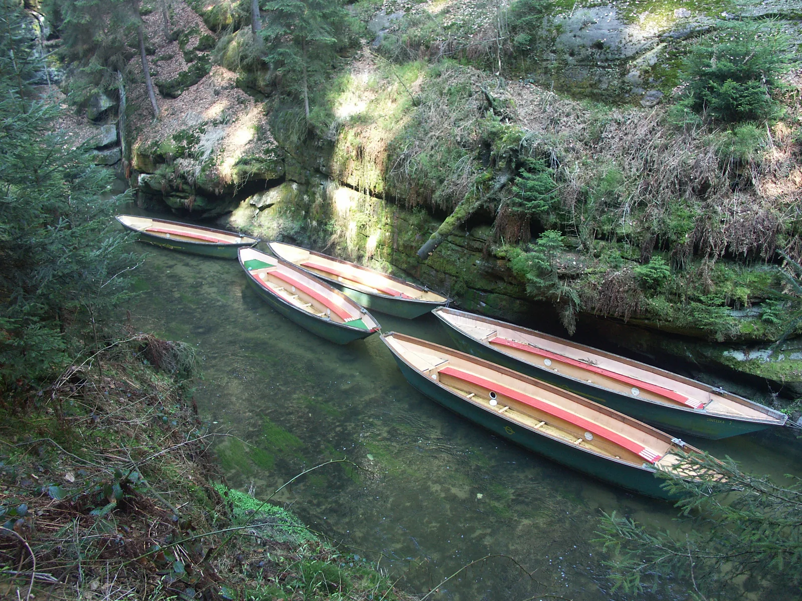 Fünf leere Holzkähne liegen nebeneinander an der Anlegestelle in der Edmundsklamm, dahinter eine bewachsene Felswand