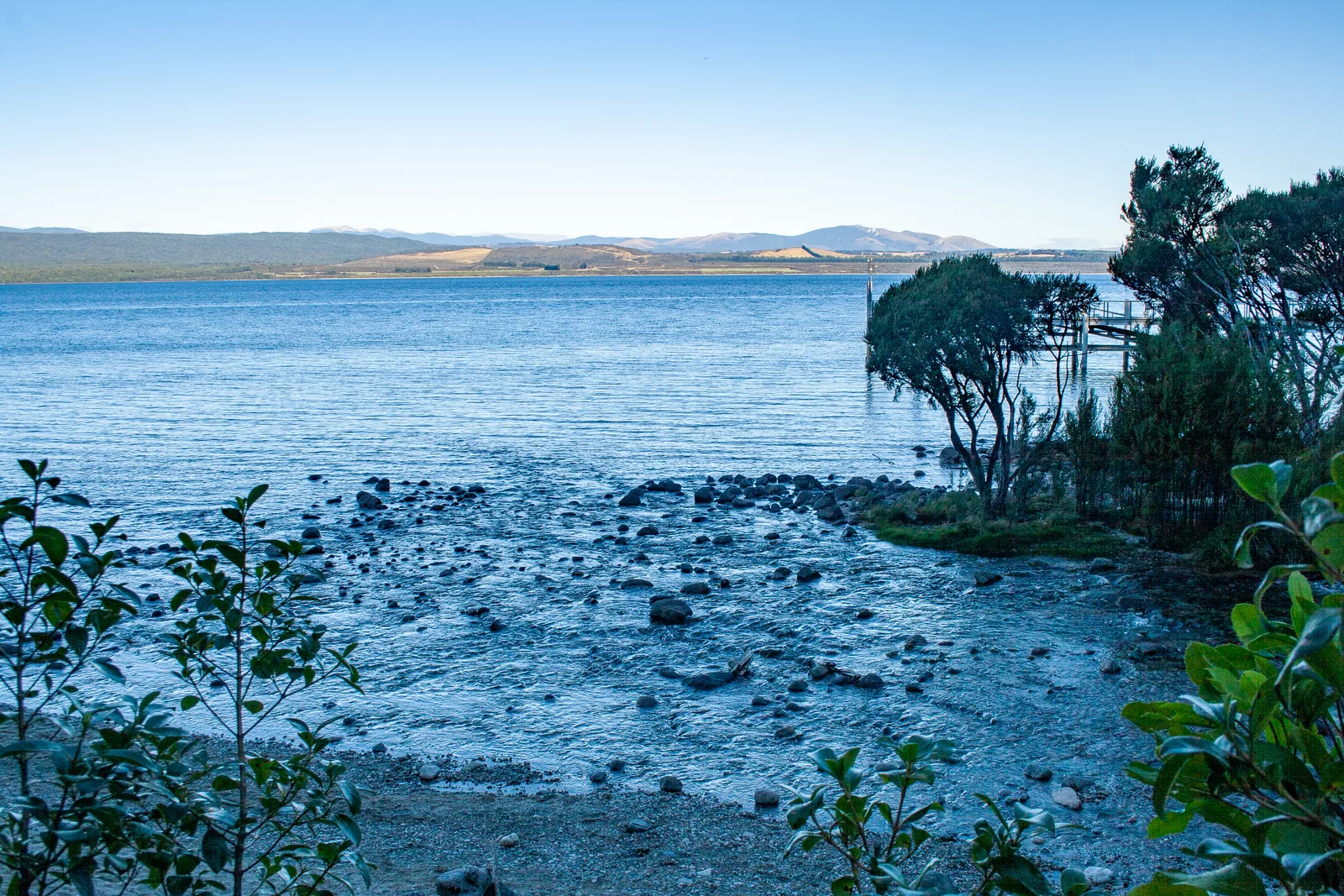 Steiniges Ufer des Lake Te Anau an den Glühwürmchenhöhlen im Fiordland-Nationalpark, im Hintergrund das flache Ostufer des Sees