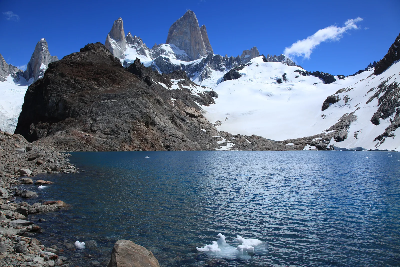 Der Fitz Roy im Nationalpark Los Glaciares über der Laguna de los Tres, davor ein dunkler Felsrücken und Schneefelder unter blauem Himmel