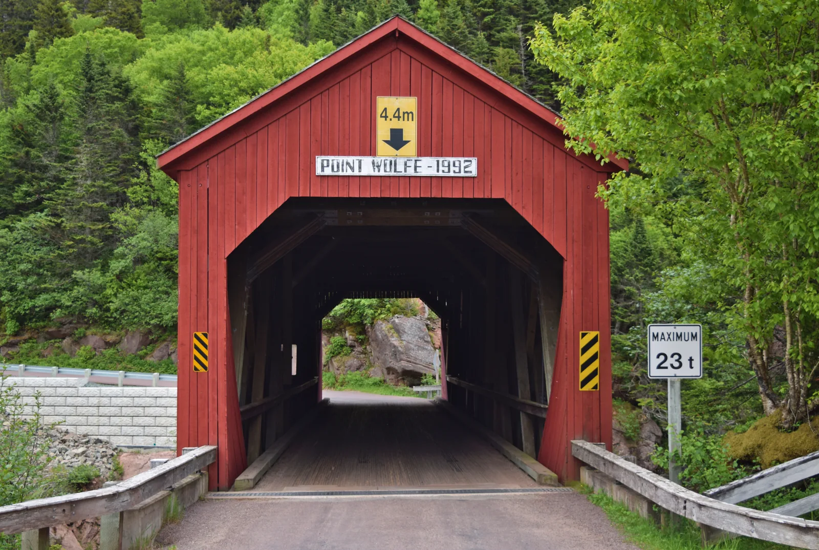 Die rote überdachte Holzbrücke am Point Wolfe von vorn, mit Höhen- und Lastbeschränkung am Portal, ringsum dichter Wald