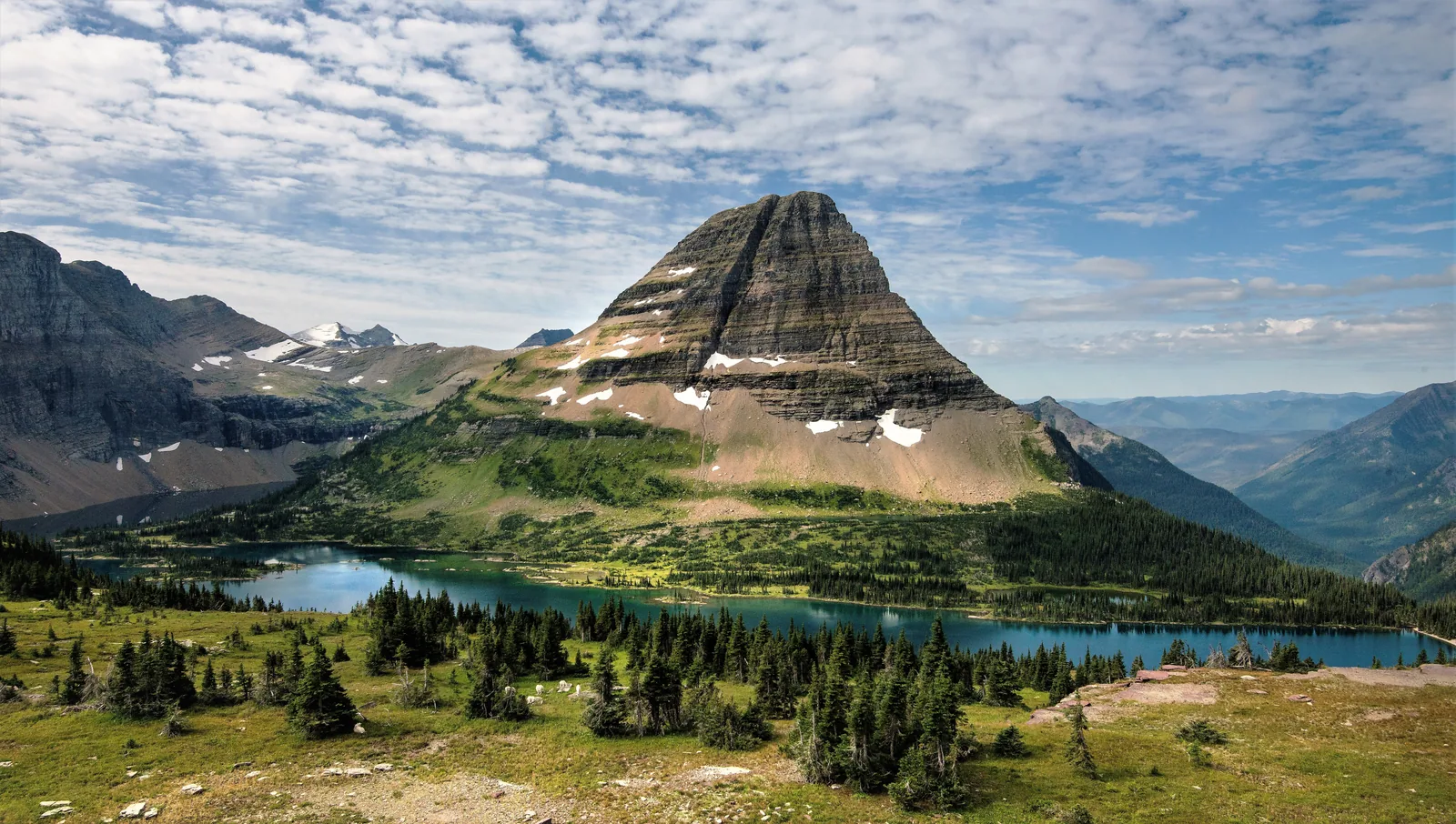 Der türkisfarbene Hidden Lake unterhalb des pyramidenförmigen Bearhat Mountain, im Vordergrund alpine Wiesen und Nadelbäume