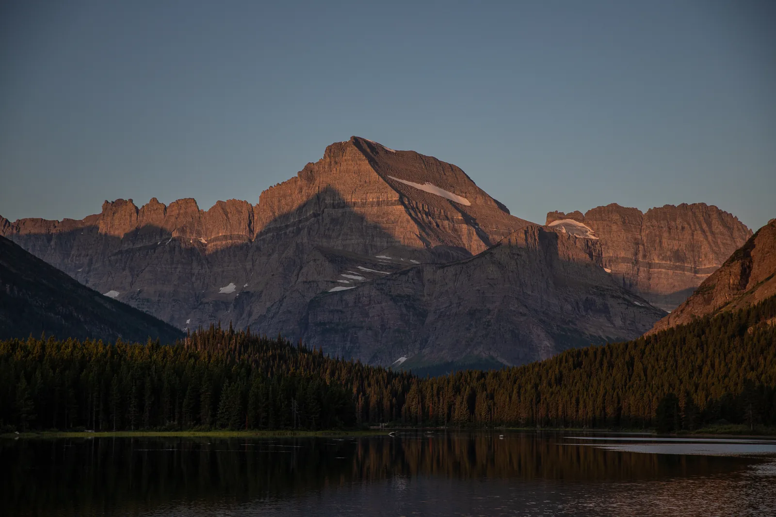 Sonnenaufgang über dem Swiftcurrent Lake, die gegenüberliegenden Berghänge leuchten rot, gesehen vom Many Glacier Hotel