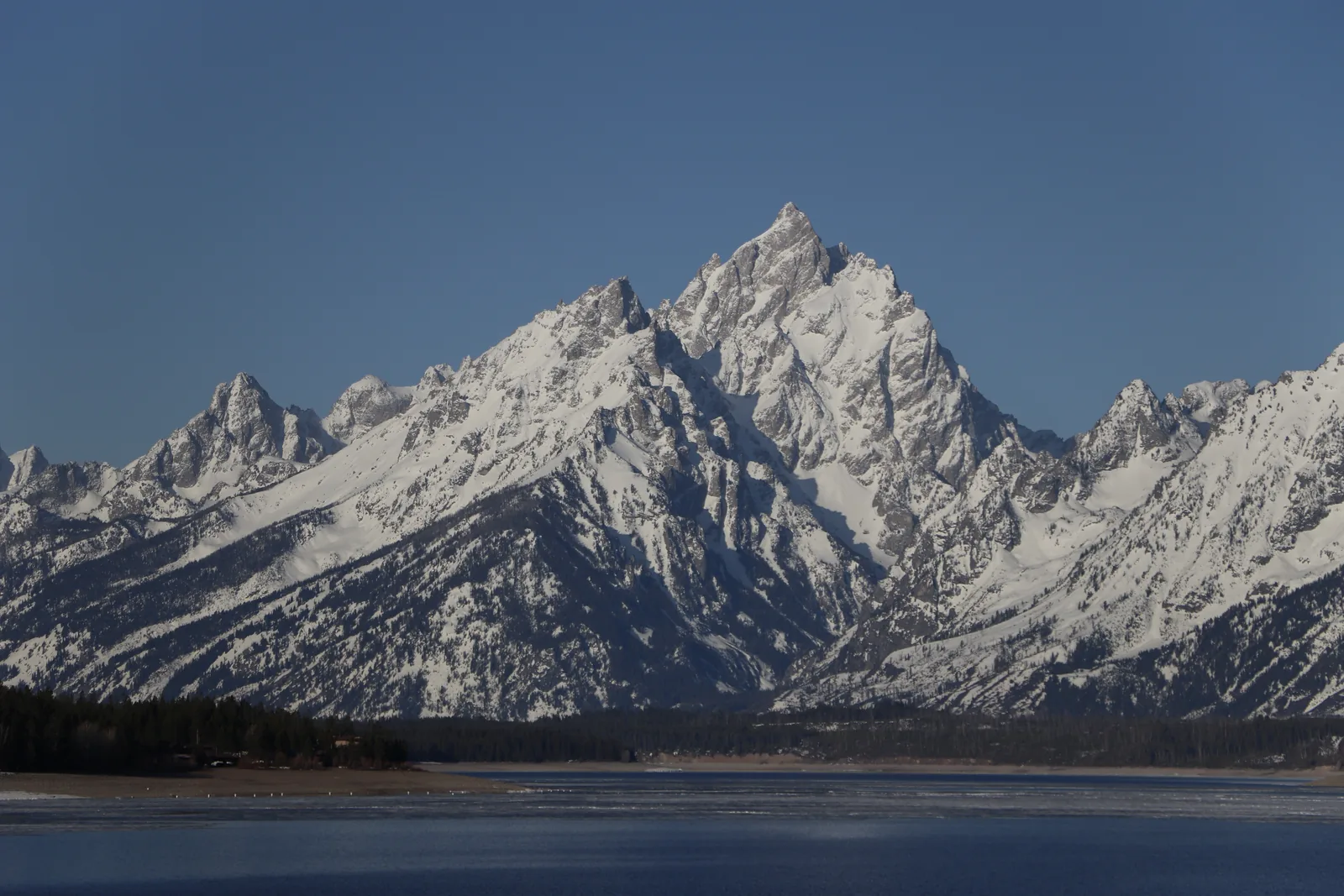 Die schneebedeckte Cathedral Group über dem auftauenden Jackson Lake mit Eisschollen im Vordergrund