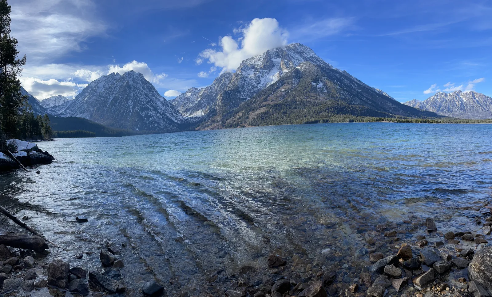 Das klare Flachwasser am Ufer des Jackson Lake, dahinter die Teton Range unter blauem Himmel