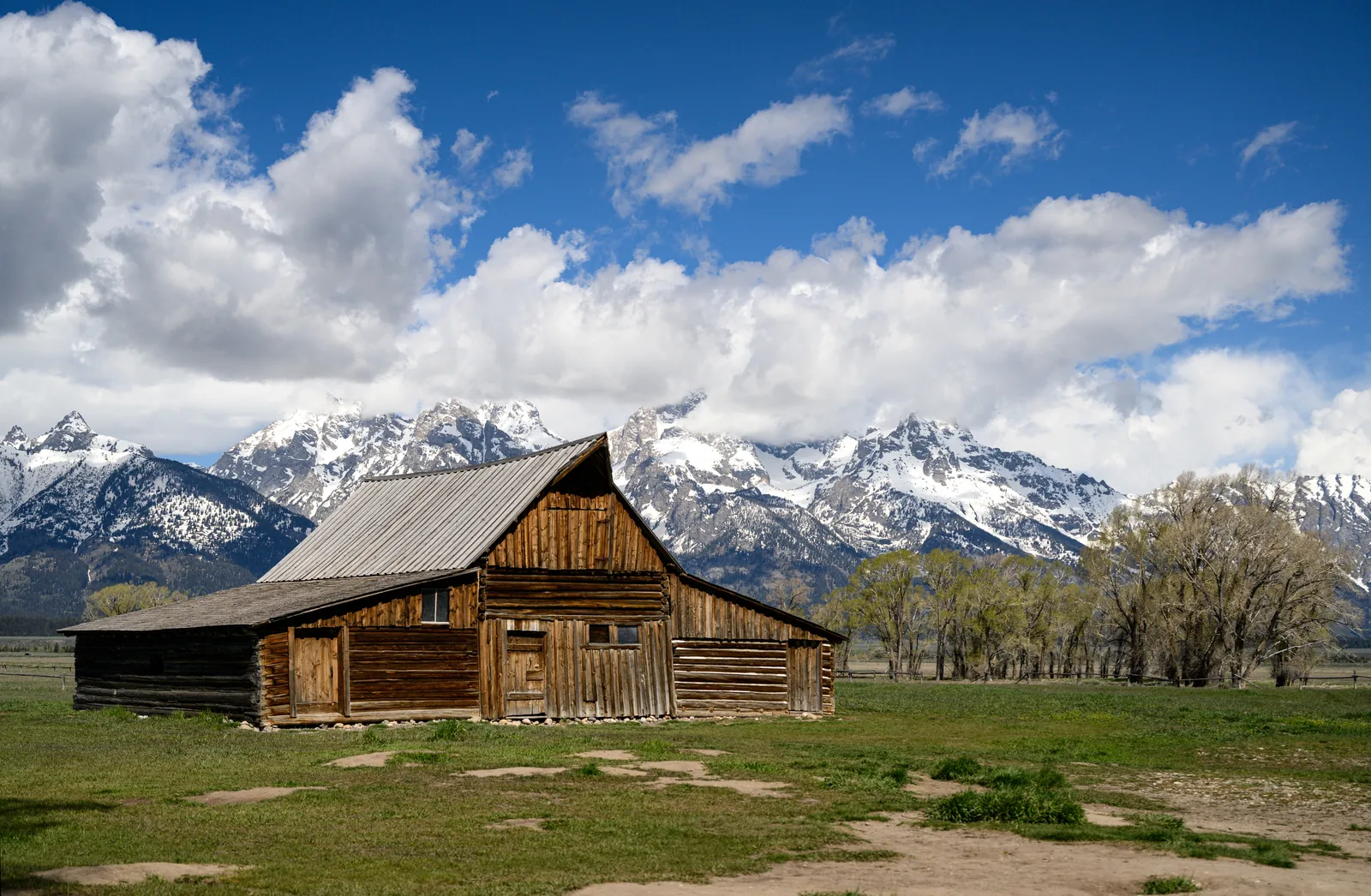 Die hölzerne Moulton-Scheune auf offener Wiese, dahinter die schneebedeckte Teton Range unter Quellwolken