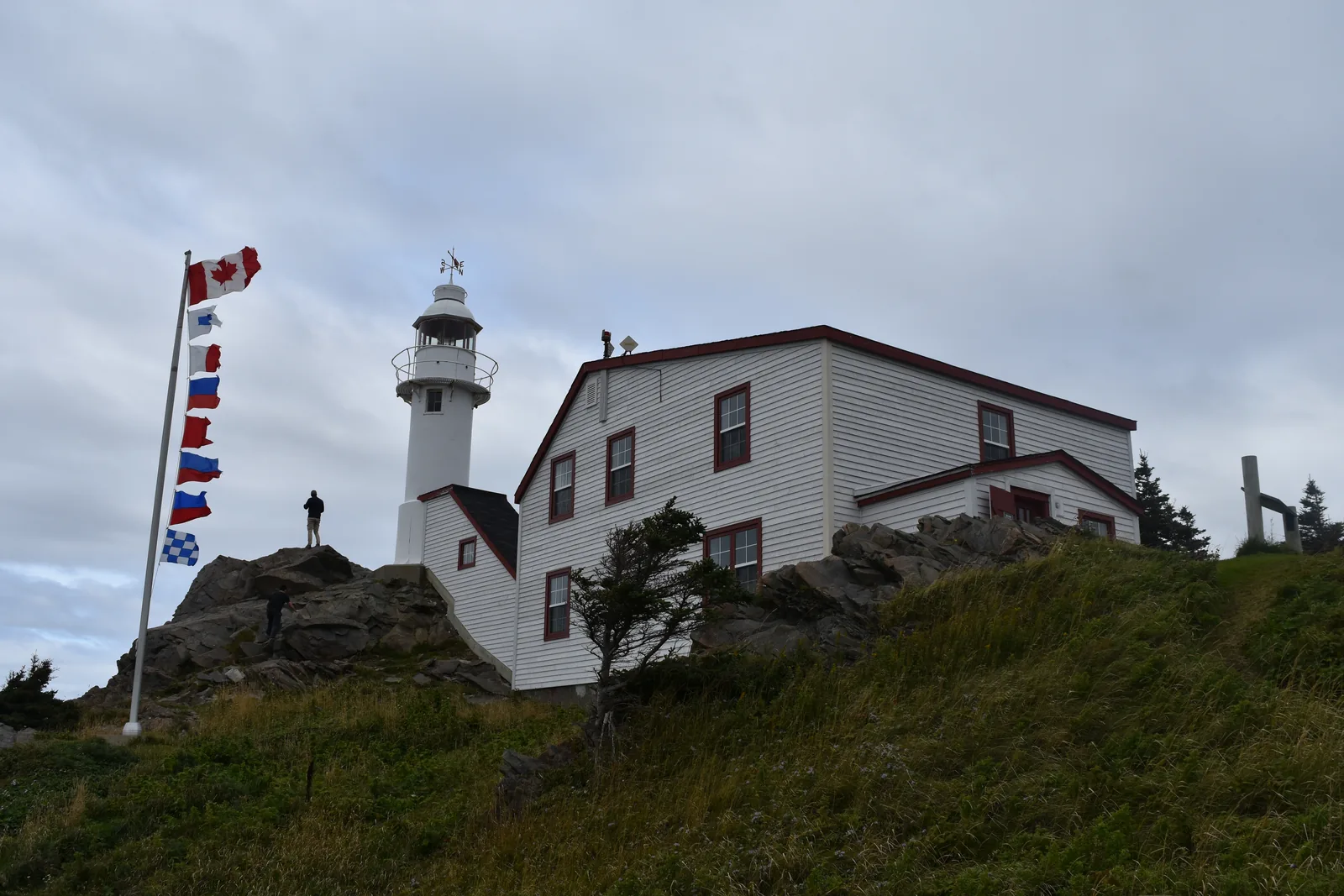 Der weiße Leuchtturm von Lobster Cove Head mit dem Wärterhaus auf einem Felskopf, davor ein Fahnenmast mit Signalflaggen