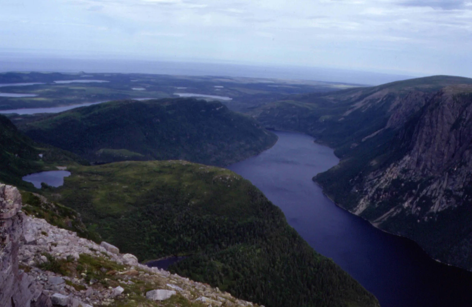 Blick vom Gipfelplateau des Gros Morne hinab auf den schmalen, dunklen Ten Mile Pond zwischen steilen, bewaldeten Talflanken