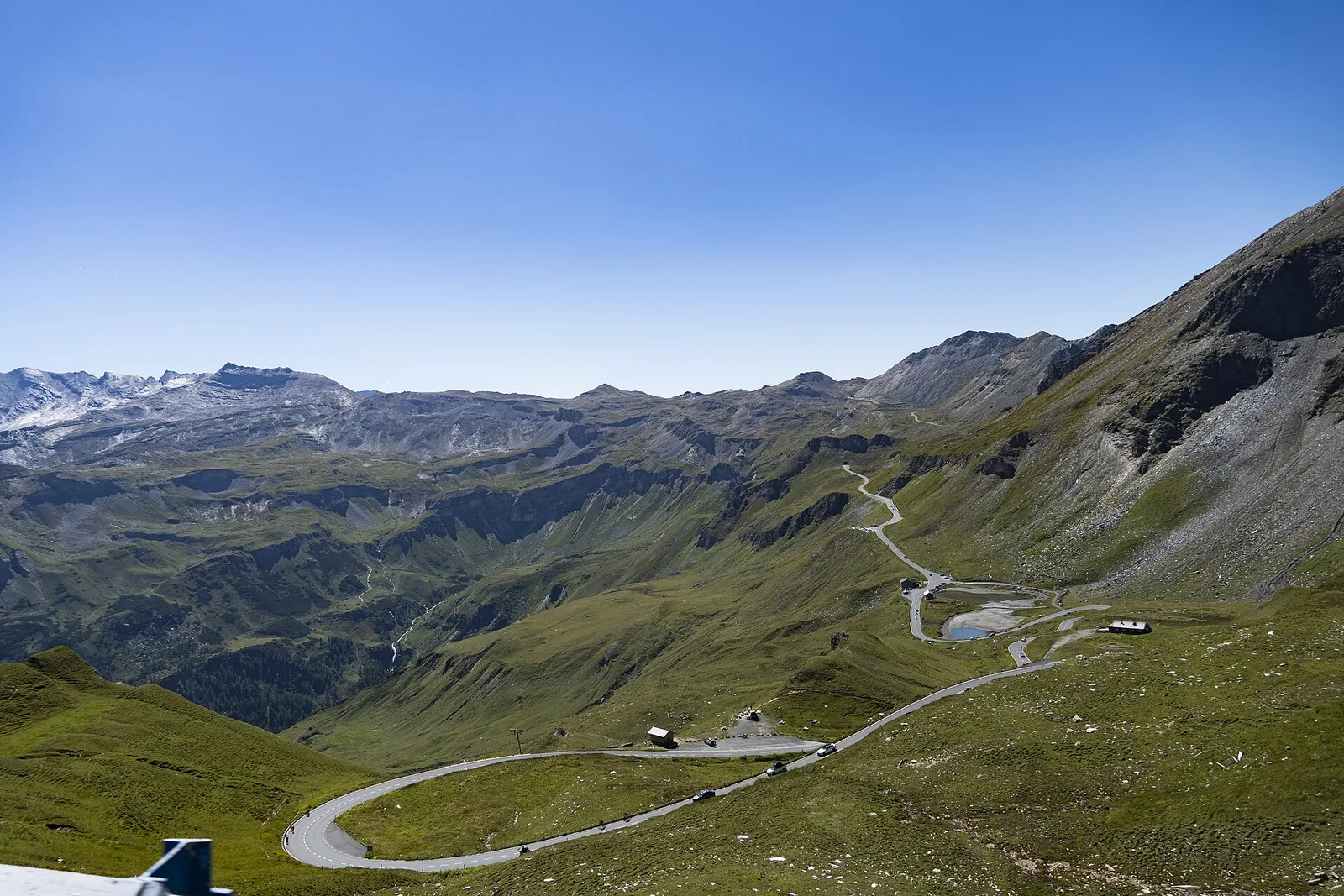 Großglockner Hochalpenstraße in weiten Kurven durch grüne Almhänge, im Hintergrund die Fuscher Lacke