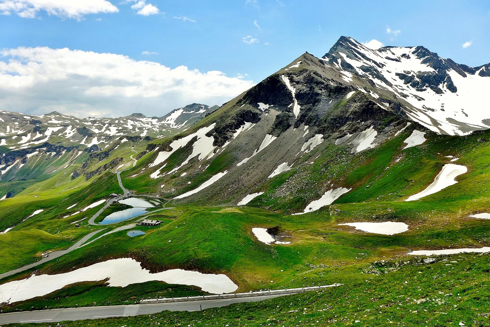 Grüne Hänge mit Schneeresten und Gipfel der Hohen Tauern, aufgenommen nahe dem Fuscher Törl an der Großglockner Hochalpenstraße