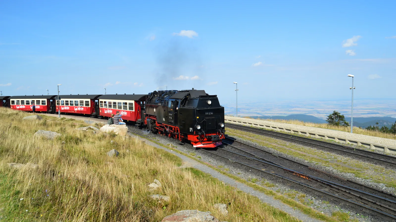 Dampfzug der Brockenbahn am Bahnhof auf dem Gipfel unter blauem Himmel