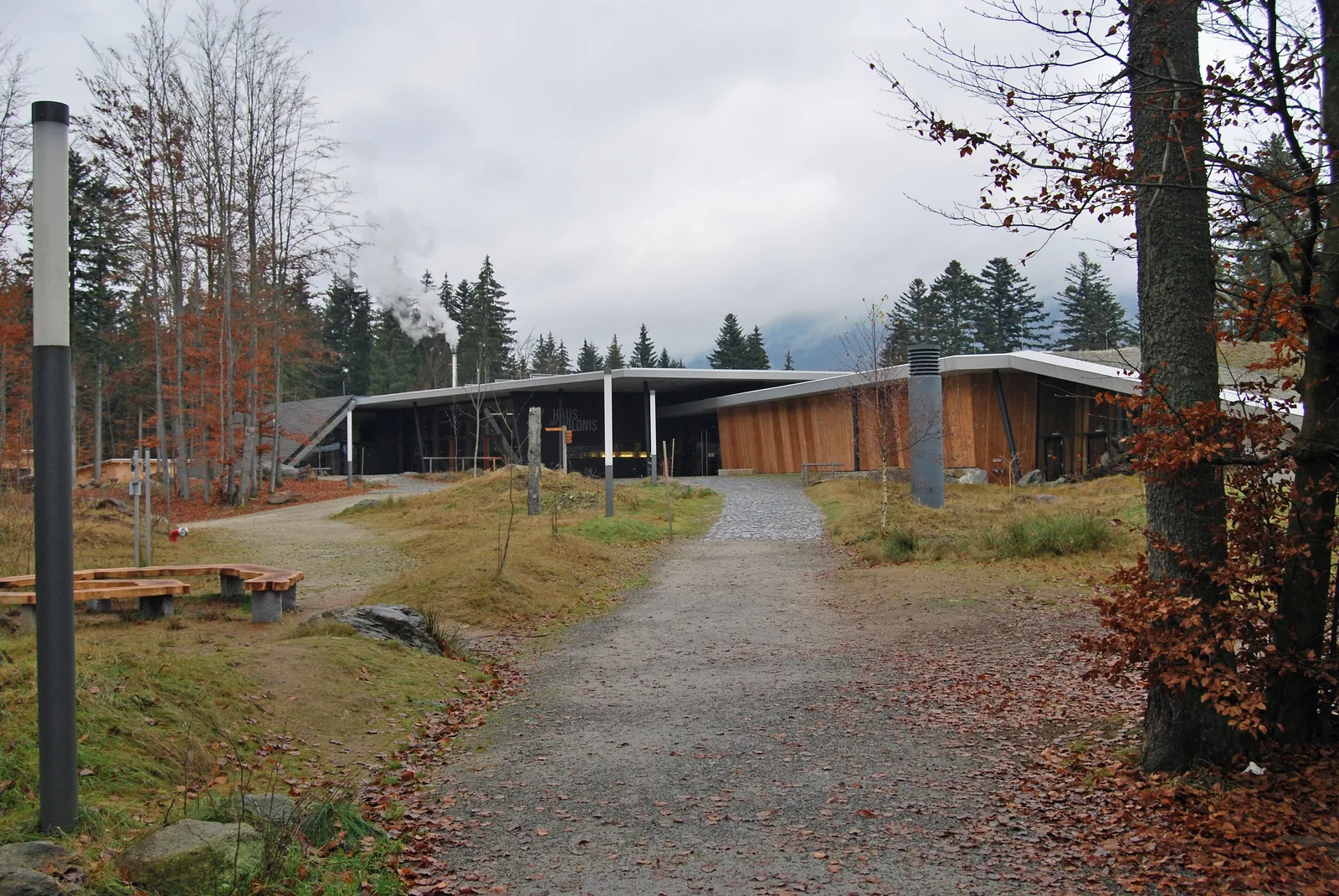 Schotterweg durch herbstliches Gelände zum flachen Holzbau des Hauses zur Wildnis bei Ludwigsthal