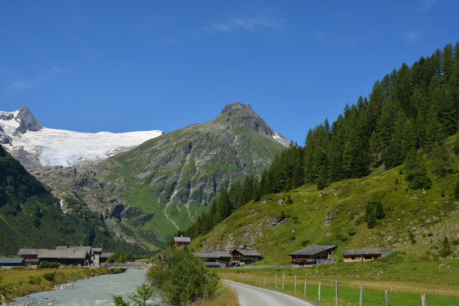 Almhütten von Innergschlöß am Bach, dahinter ein Gletscher unter felsigen Gipfeln