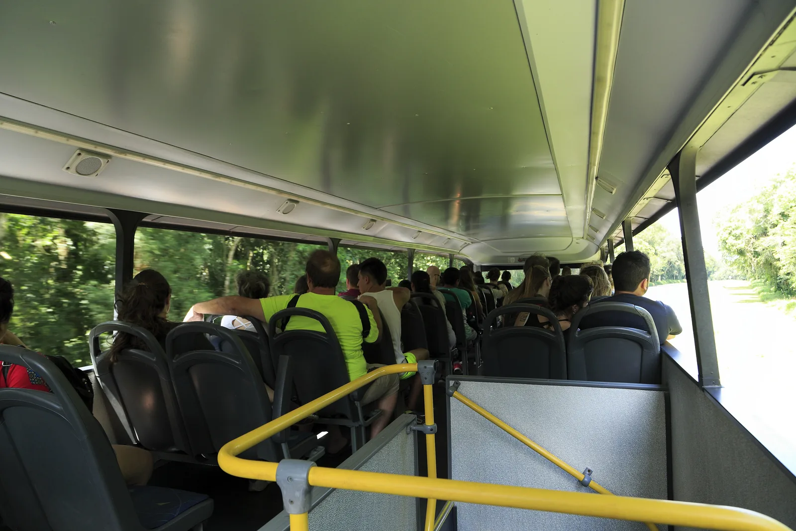 Im oberen Deck eines offenen Doppelstockbusses im Iguaçu-Nationalpark sitzen Fahrgäste, draußen Wald