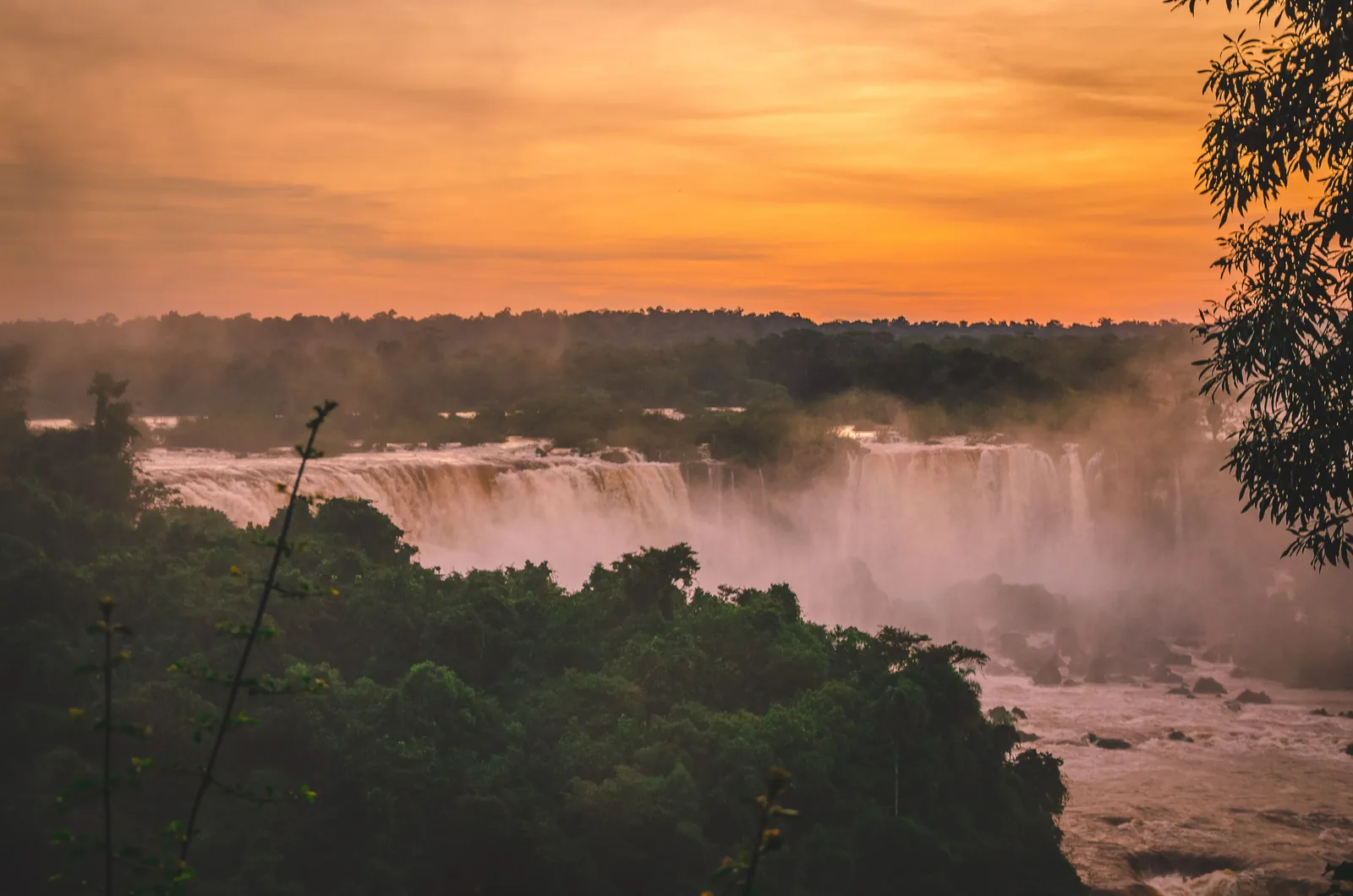 Orangefarbener Abendhimmel über den Iguaçu-Fällen, der Wald davor liegt schon im Schatten