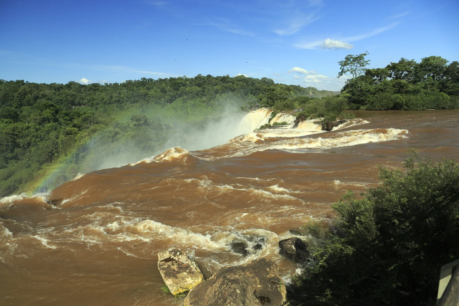 Braunes Hochwasser des Iguazú stürzt am Salto San Martín über eine breite Kante, im Hintergrund dichter Wald