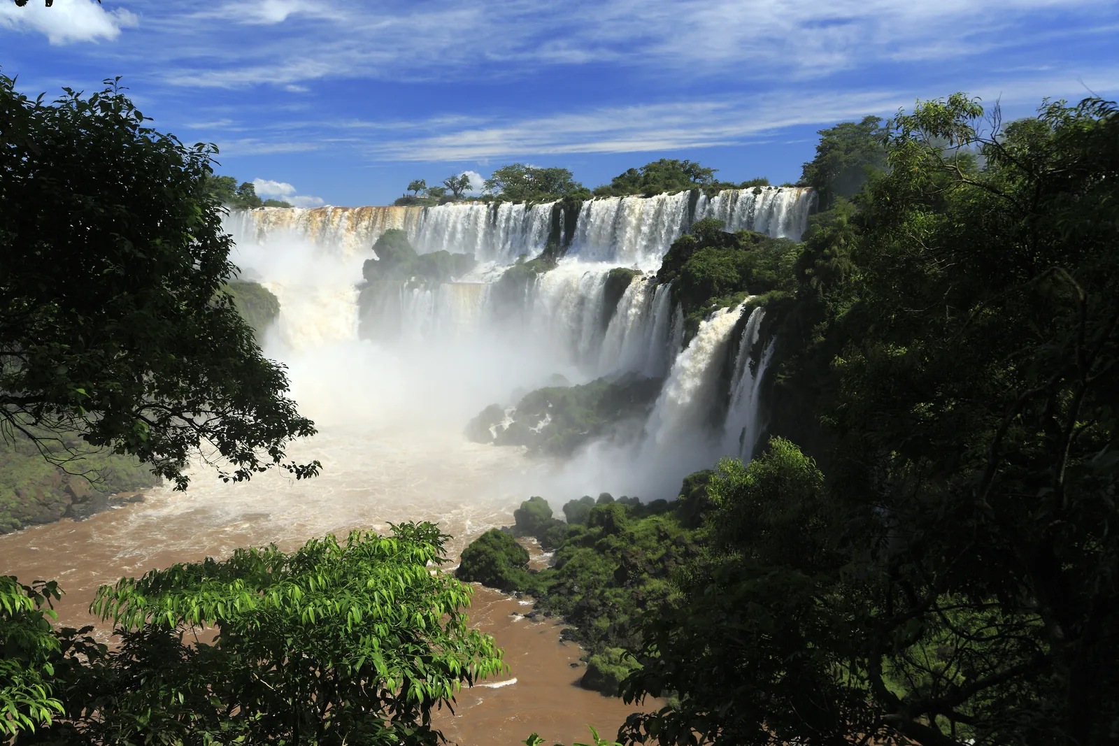 Vom unteren Rundweg im Iguazú-Nationalpark blickt man zwischen Bäumen auf die weißen Fälle Adán y Eva und Bossetti, unten tost braunes Wasser