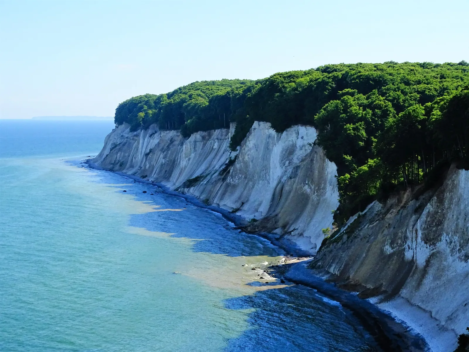 Weiße Kreidefelsen mit Buchenwald auf der Kante, darunter das türkisfarbene Ostseewasser