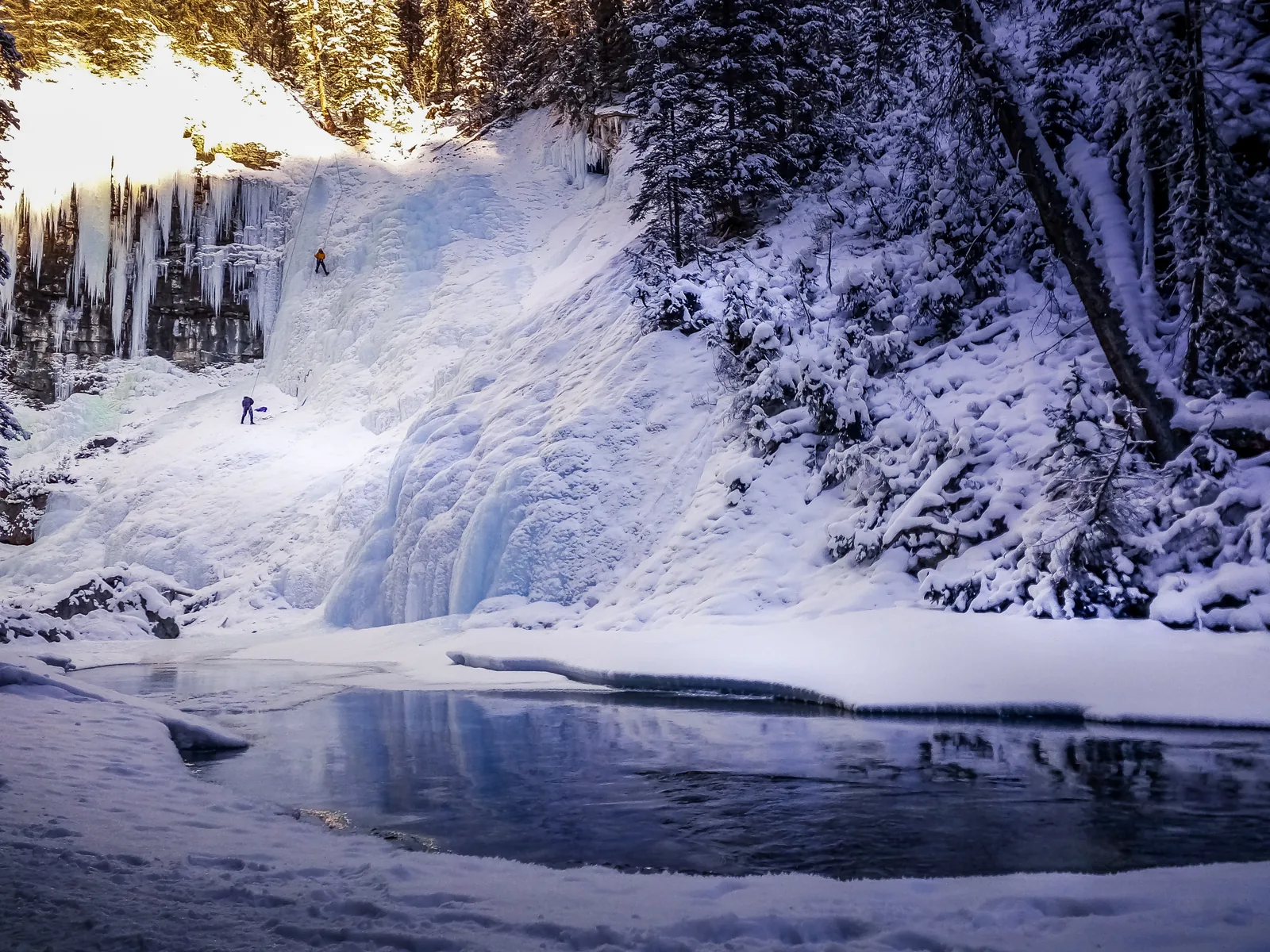 Gefrorener Wasserfall im Johnston Canyon mit Eiskletterern, davor verschneiter Bach